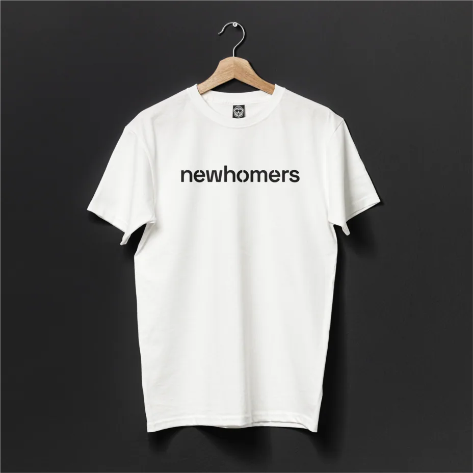 Weißes T-Shirt mit newhomers-Logotyp auf einem Bügel vor einer dunklen Wand