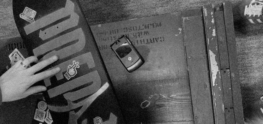 Schwarz-Weiß-Foto eines PREPARE-Skateboards und eines Retro-Handys auf einer Holzkiste